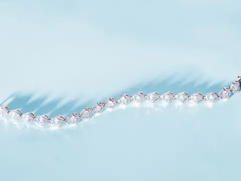 A diamond line bracelet laid in a curve on a pale blue ground