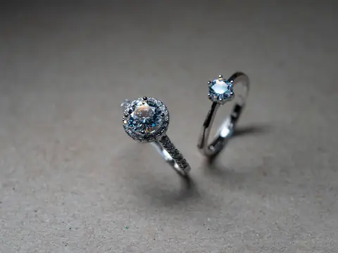 Two white gold diamond rings, a halo and a six-prong solitaire, on grey card