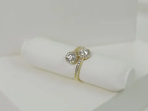 A yellow gold ring with two round diamonds in halos, on a white ring roll