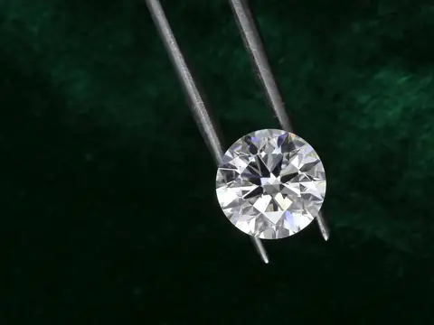 A round brilliant diamond held in steel tweezers against dark green velvet