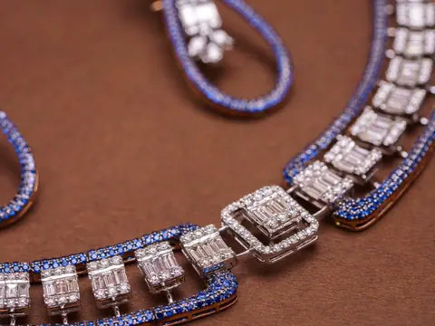 A white gold necklace of square baguette diamond links edged with small blue stones, and a matching earring, on brown card