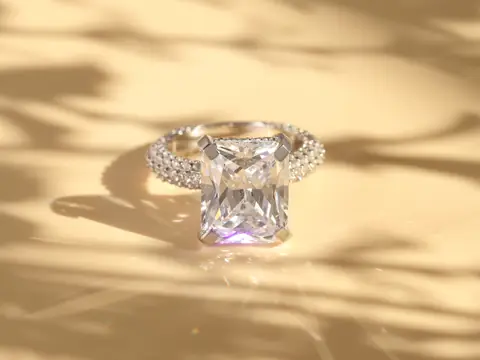 A ring with a large emerald-cut diamond on a sunlit cream surface