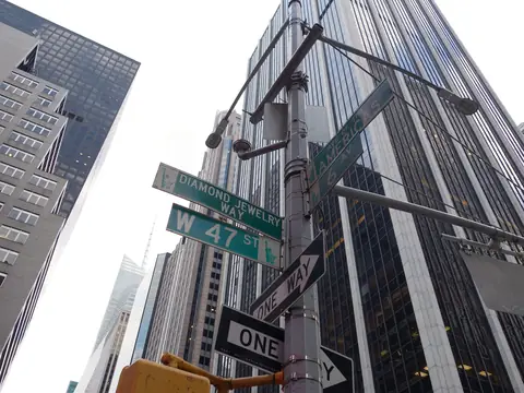 Green street signs for W 47 St and Diamond Jewelry Way on a lamp post at Sixth Avenue, with Midtown towers behind