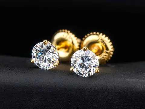 A pair of round brilliant diamond stud earrings in yellow gold prongs on black velvet