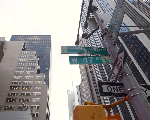 Green W 47 St and Diamond Jewelry Way street signs on a lamp post at Sixth Avenue, below the glass towers of Midtown