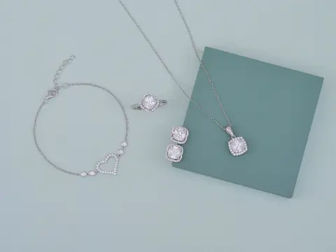 A white gold diamond set laid flat: a bracelet, a cushion-cut ring, earrings and a pendant on a pale green ground