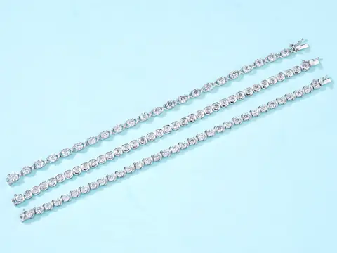 Three diamond tennis bracelets laid side by side on a pale blue ground