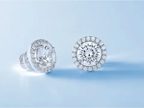 A pair of round diamond halo stud earrings on a pale blue ground