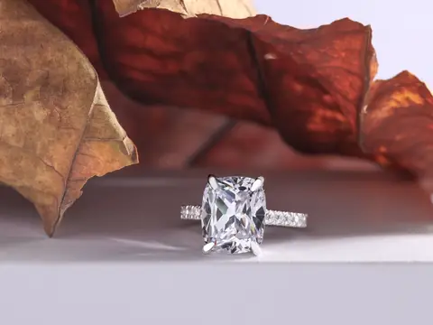 A ring with a large cushion-cut diamond on a white surface beside dried leaves