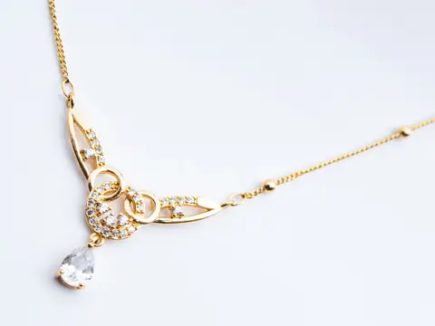 A yellow gold necklace with a pear-shaped diamond drop on a white ground